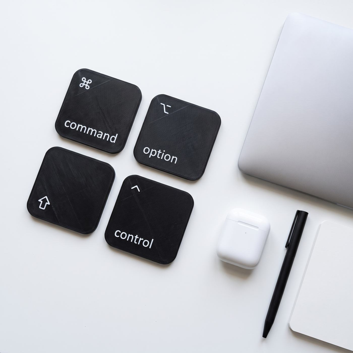 From above: the four coasters two by two on a white desk beside a laptop, earbuds and a pen.