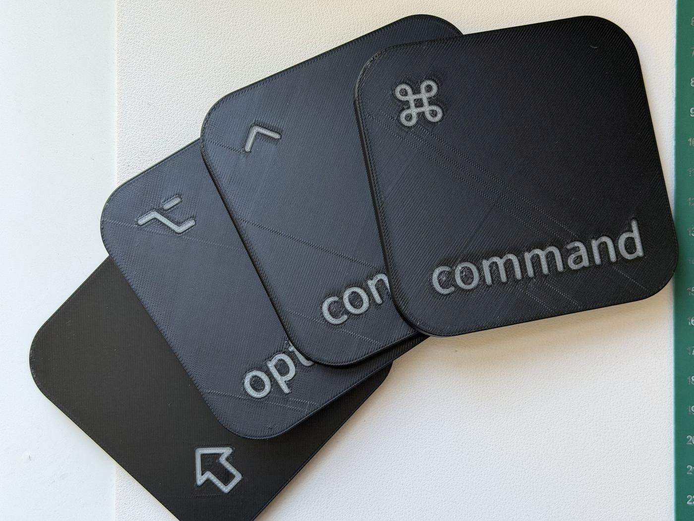 Our printed coasters fanned out on a cutting mat: command, control, option and shift, black with silver legends.