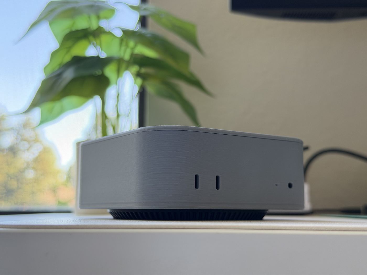 The Mac mini holder on an oak desk by a window, the option coaster in front of it and a cup of coffee on the command coaster, a keyboard in the corner.